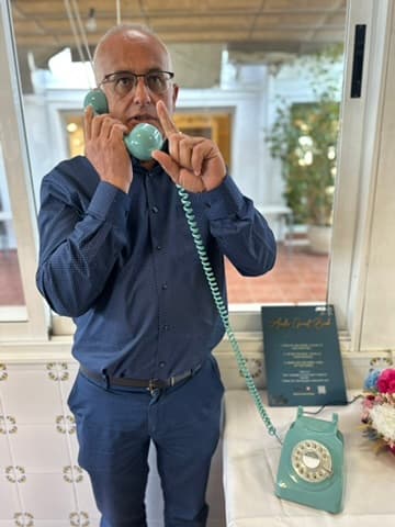 A guest leaving a message on a teal rotary telephone, with the instruction sign beside him