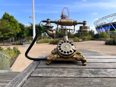 An ornate brass candlestick telephone on a wooden bench